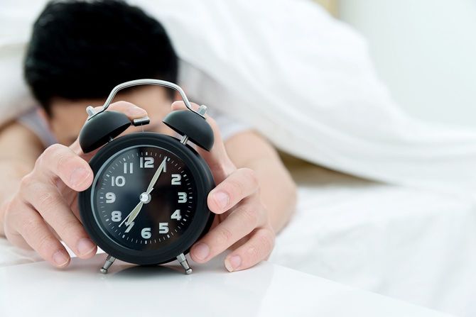目覚まし時計を止めるために手を伸ばす人