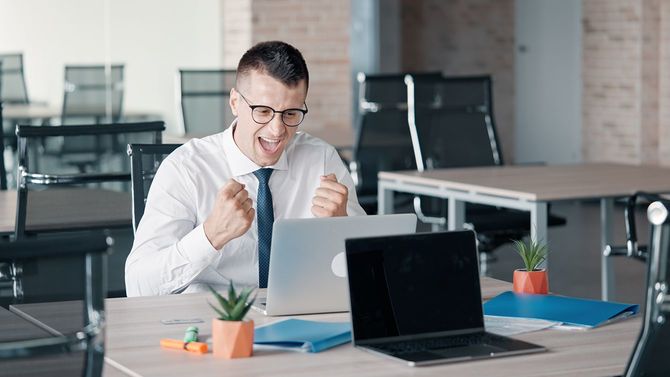 彼のオフィスに座って、ラップトップを見て、とても幸せに感じる白人のビジネスマン