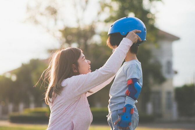 アジアの母が彼女の息子を助けて身に着けている青いヘルメット楽しむ時間一緒に公園で