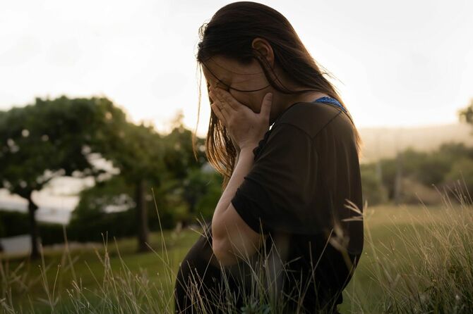 野原で手で顔を覆い泣いている妊婦