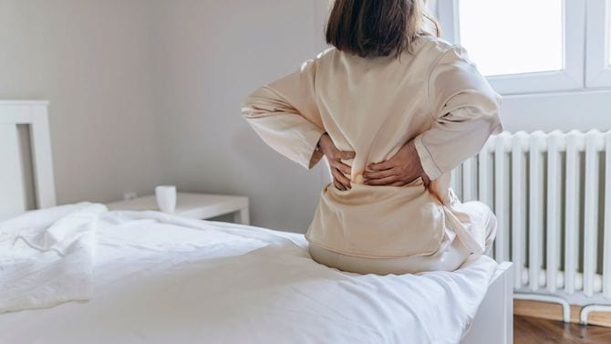起き抜けにベッドに座り、痛む腰を押さえる女性