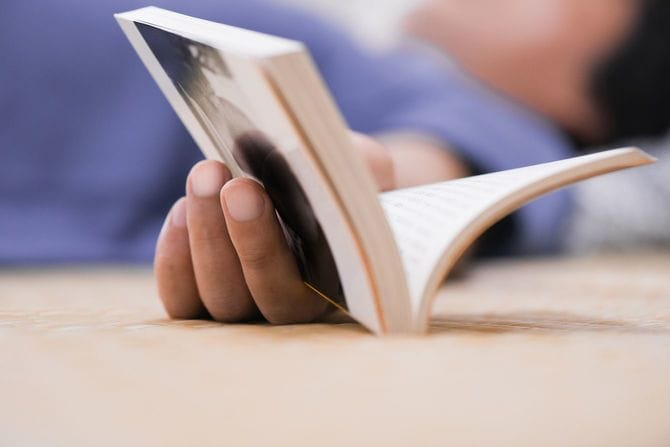 文庫本を手に仰向けになる男性の手元