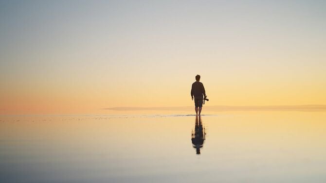 夕暮れ時にカメラを持って浅瀬を歩く一人旅の男性