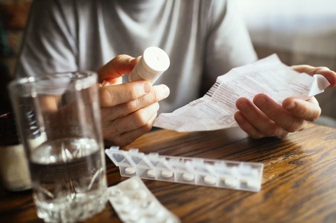 薬に添付された注意書きを読んでいる男性