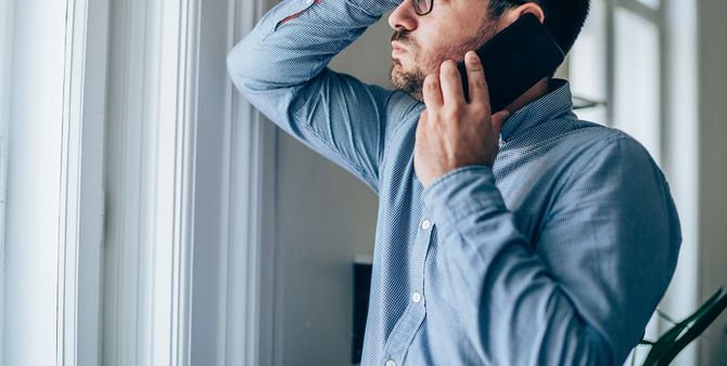 オフィスで携帯電話で話している額に手をあてたビジネスマン