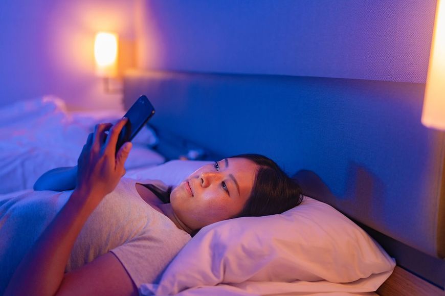寝る前にベッドでスマホを見ている女性