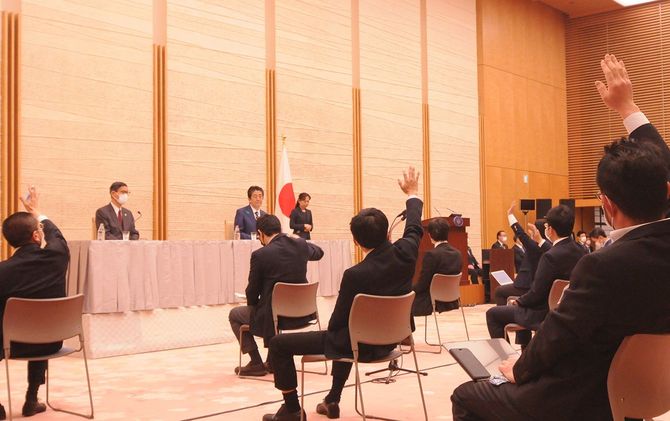 安倍首相の記者会見で挙手をする記者。司会進行をする内閣広報官から指名されれば質問できる。