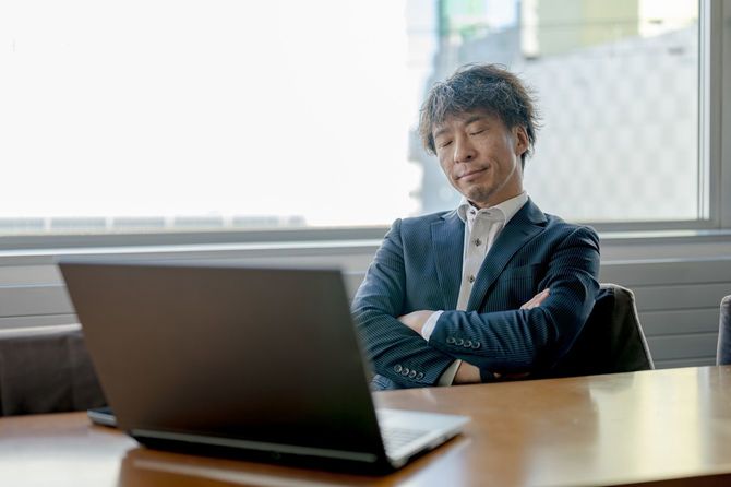 ラップトップの前で、目を閉じて腕を組んでいる男性