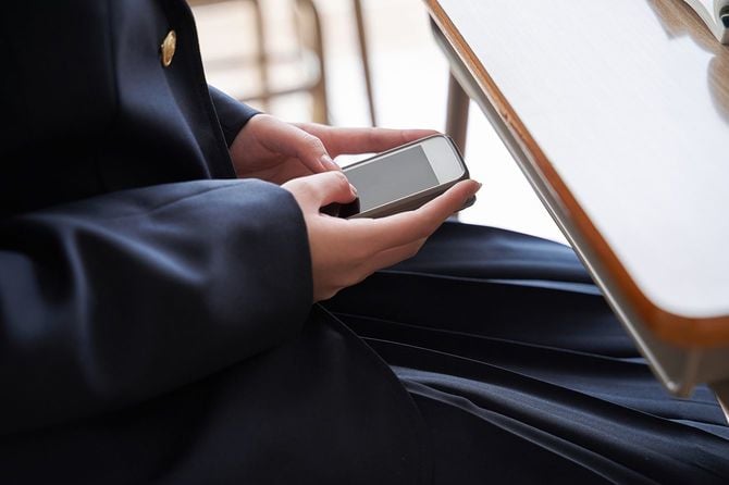 携帯電話を操作するために教室に隠れている日本の中学生