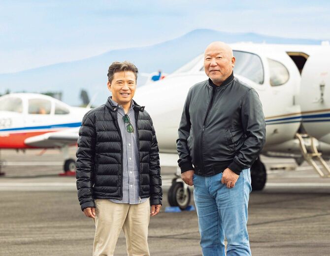 駐機場で並ぶ山中さんと西村さん、背景には飛行機が停まっている