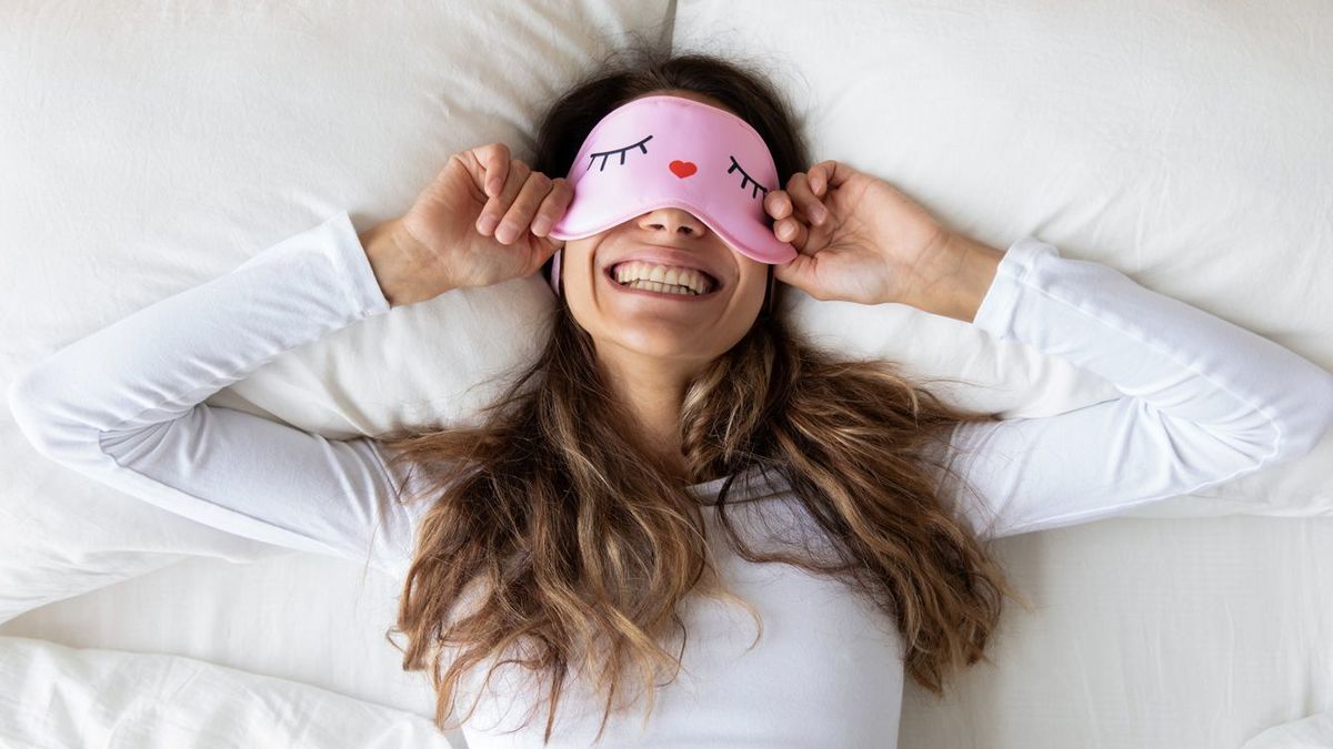 寝ながらアイマスクを付けて笑う女性