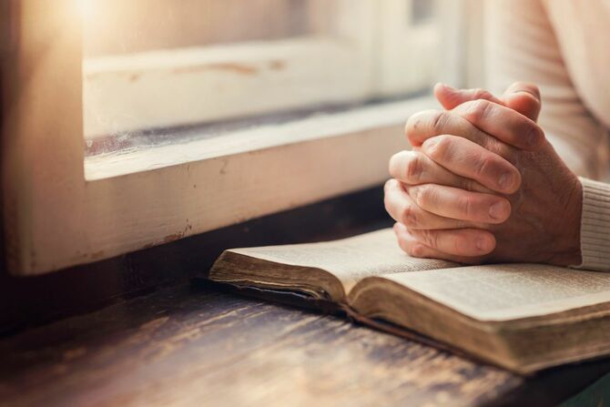 窓辺で聖書の上に手を置いて祈る女性