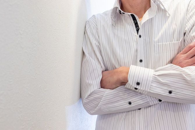 白いシャツを着て壁にもたれかかり、腕を組んでいる男性