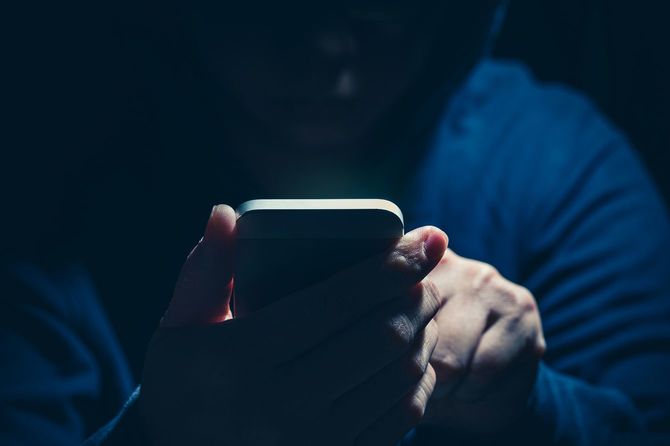 フードを被った人がスマートフォンを使用している