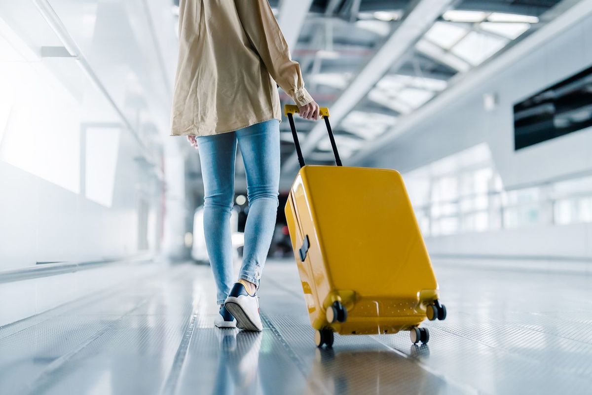 空港ターミナルをスーツケースをひいて移動する女性の後ろ姿