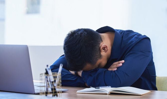 オフィスの机で寝ている若いビジネスマン