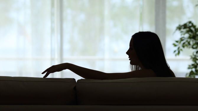 パートナーを失って一人ソファーに座り手を伸ばす女性のシルエット