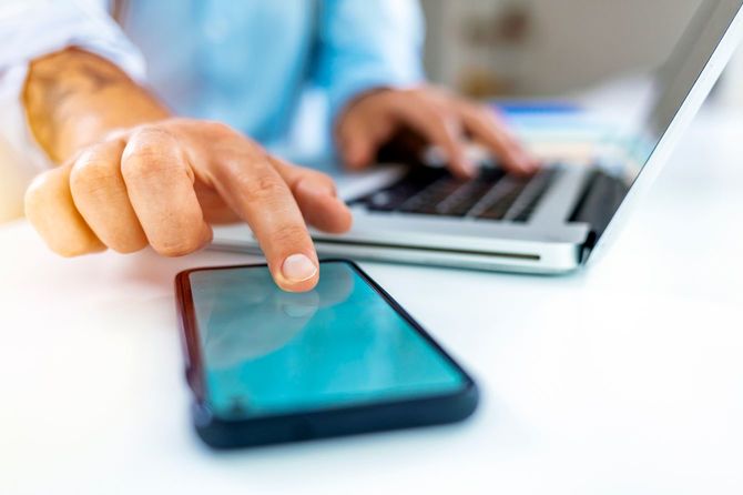 コンピュータで作業しながら携帯電話を使用しているビジネスマン