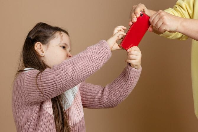 女の子の手からスマホを取り上げようとしている親