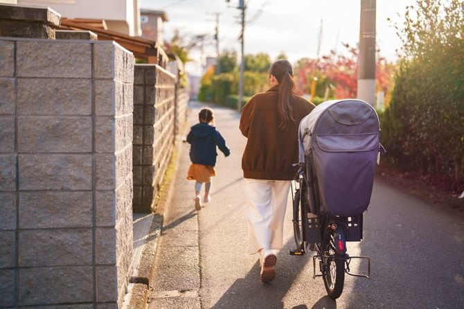 母親が自転車のそばを歩き、子どもが住宅街を先に走る