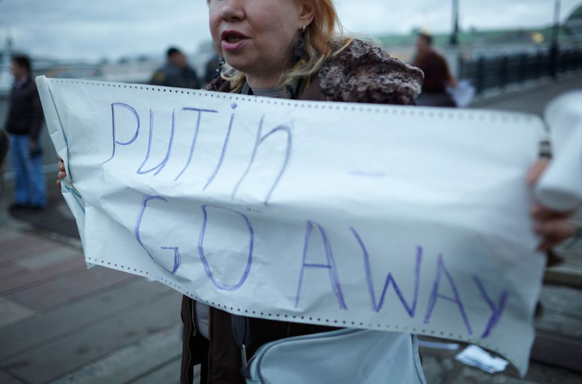 「プーチン出ていけ」の横断幕を手に持つ女性