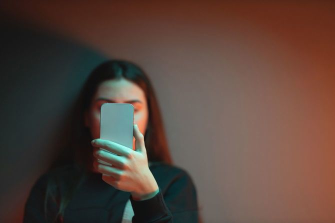 薄暗い部屋で壁にもたれ、スマートフォンを真顔で見つめている女性