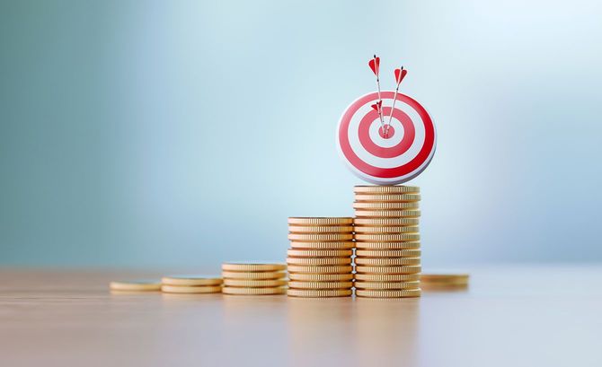 積まれたコインの上に置かれた、3本の矢が中心に刺さった的
