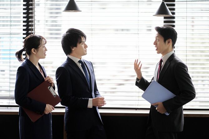オフィスで立ち話をする3人のビジネスパーソン