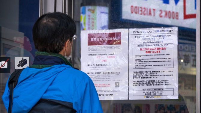 非常事態宣言による業務時間変更の店の通知を見ている日本人男性