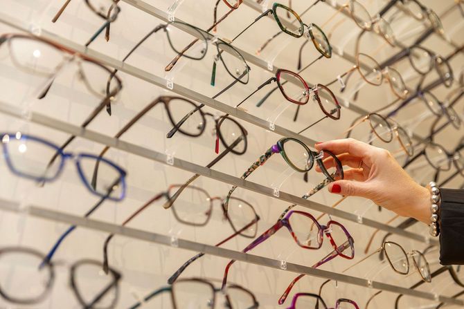 様々なメガネが並んだ眼鏡店のディスプレイと、商品を選ぶ人の手元