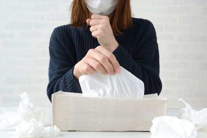 鼻をかむのにティッシュを取るマスク姿の女性