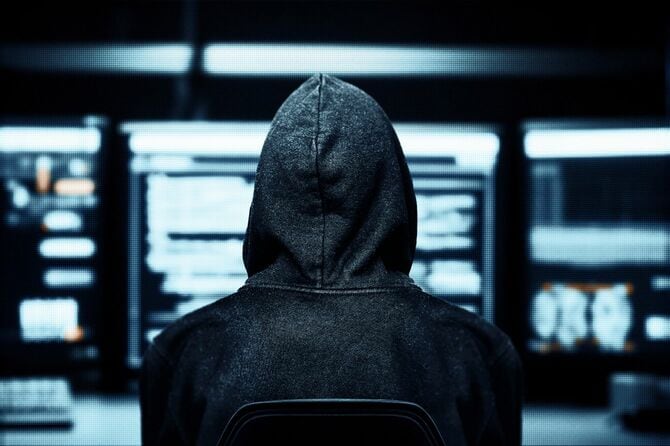 フードをかぶり、マルチモニタに向かっている人