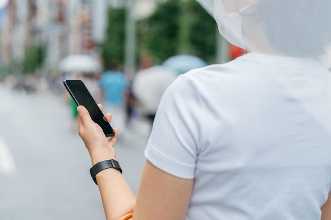 小雨が降る中歩く若い女性は、右手に傘、左手にはスマホを持ち画面を確認している