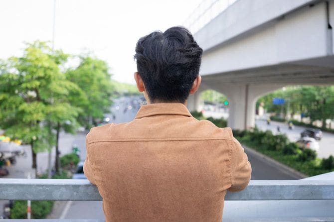 歩道橋から道路を眺めている男性の後ろ姿