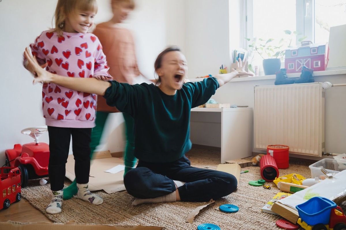 床に座ってストレスを抱える母親と周りを走る子どもたち