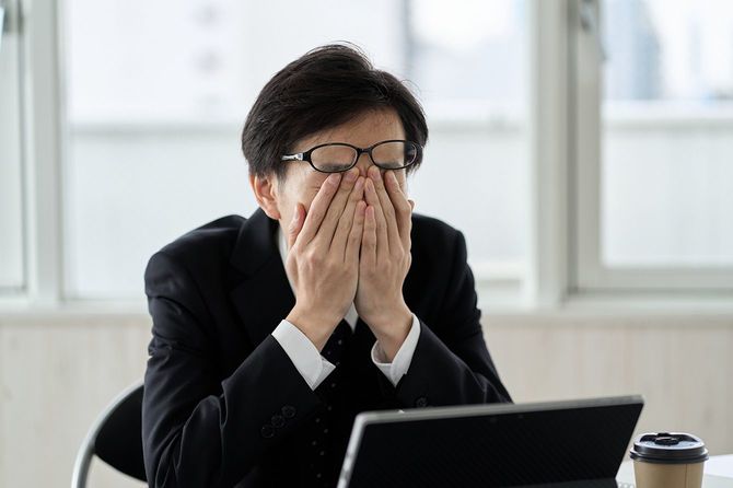 仕事の合間に疲れたように顔を覆う男性