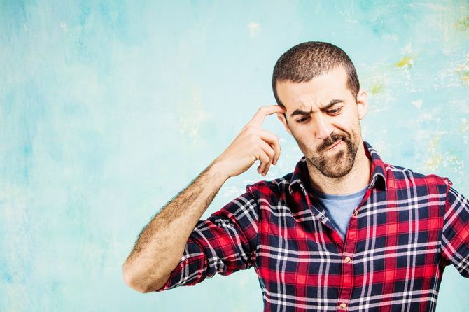 頭に指を当てて悩む男性