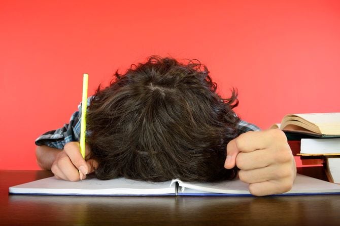 鉛筆は握りしめたまま、ノートにうつぶせになる少年