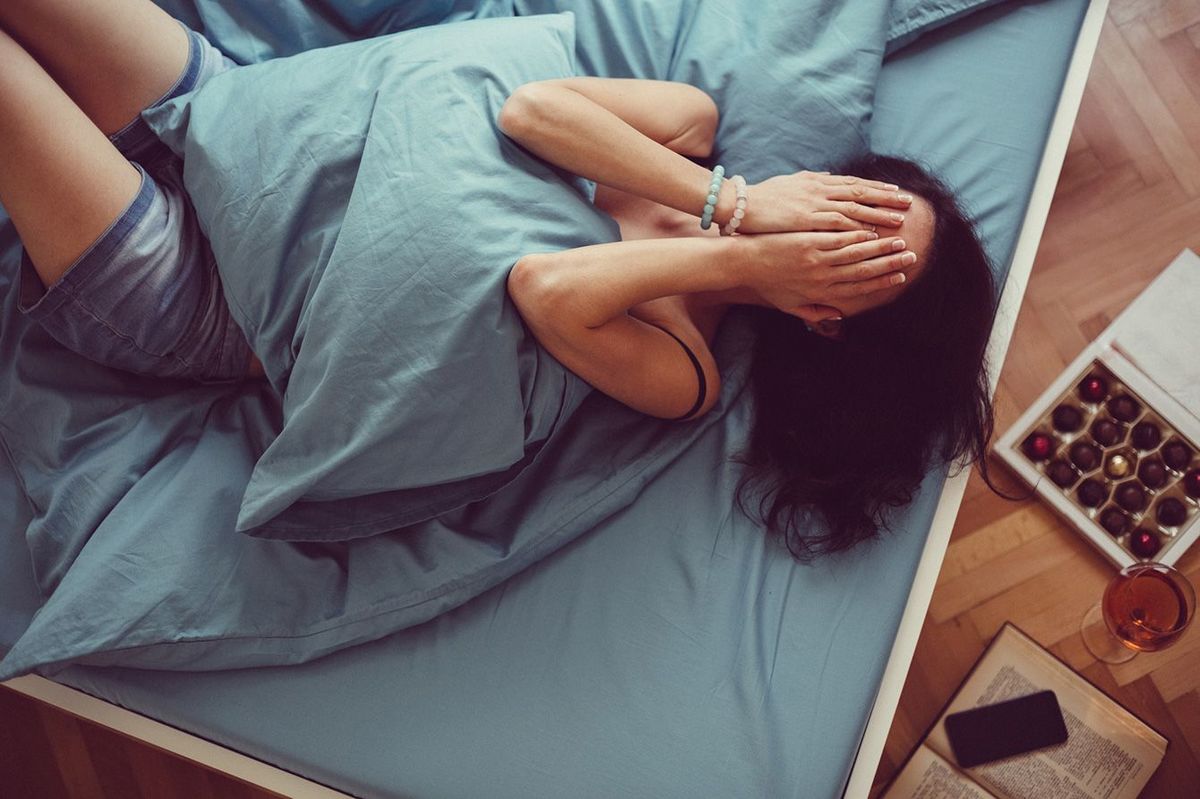 ベッドに寝転がり、手で顔を覆っている女性