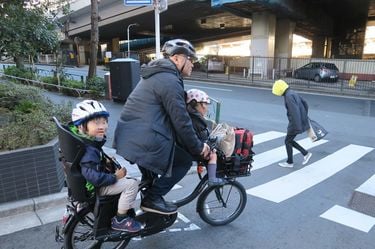 2人の子どもを自転車に乗せる筆者。自分だけでなく子どもにもヘルメットをかぶせている
