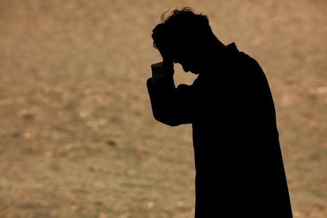 頭を抱えながら、水辺を歩いている男性のシルエット