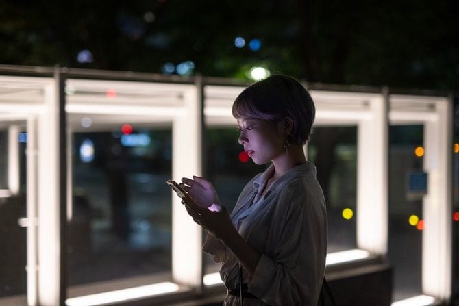 夜の街でスマートフォンを使う若い女性