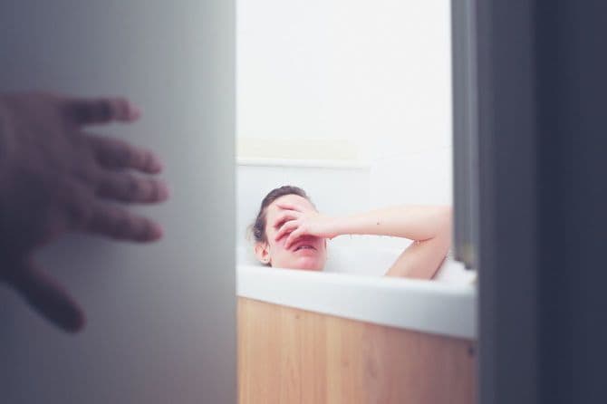 バスタブにつかる女性と浴室のドアを開けている誰かの手元