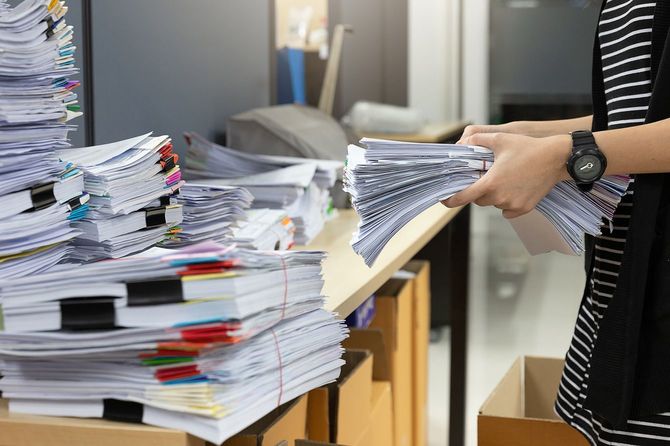 山積みの書類の前で、書類の束を持っている人