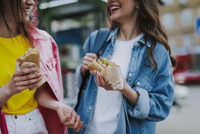 歩いてホットドッグを食べながら一緒に時間を楽しむ若い幸せなスタイリッシュな女性のトリミングされた頭の肖像画