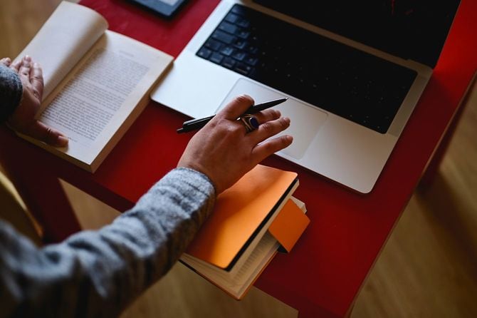 左手で書籍を開き、右手でノートパソコンを使用している人の手元