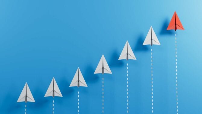 青い背景に並ぶ白い紙飛行機と一番高い位置の赤い紙飛行機