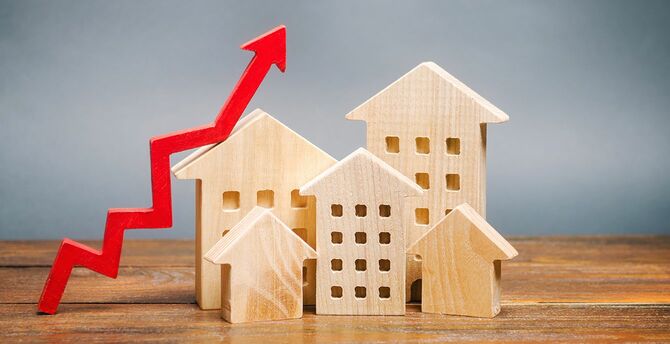 ミニチュアの木造家屋と赤い矢印アップ。住宅のコストを増やすための概念。不動産の需要が高い。家賃と住宅ローン金利の伸び。アパートの販売。人口増加