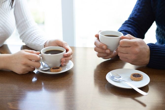 コーヒーのカップを持つ女性と男の手