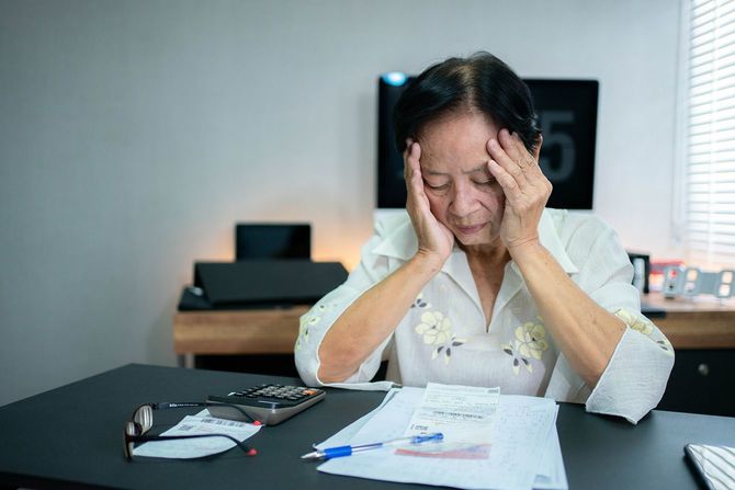 家計簿をつけながら頭を抱える高齢女性